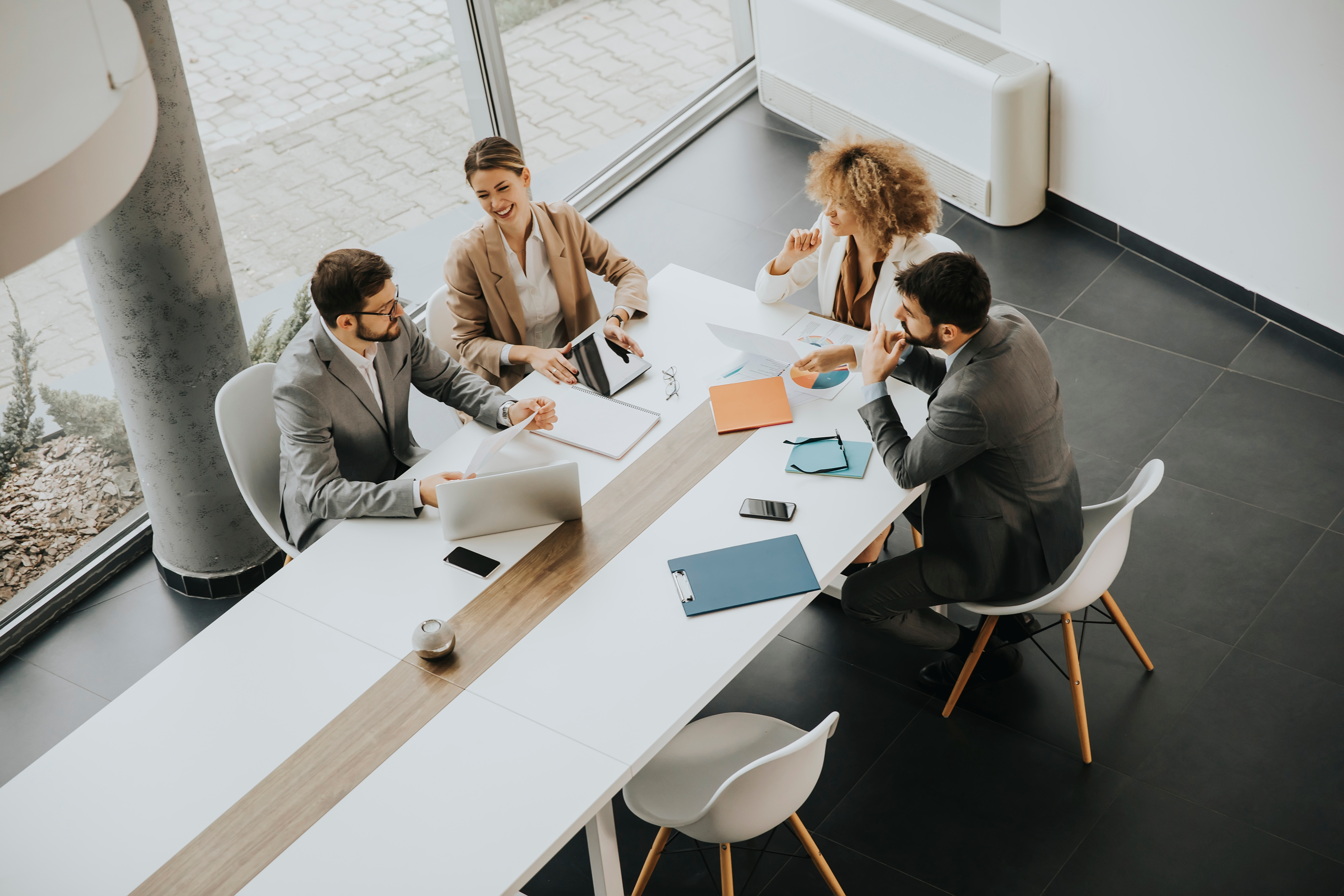 Four business professionals meeting at a white table in a modern office with laptops and notepads