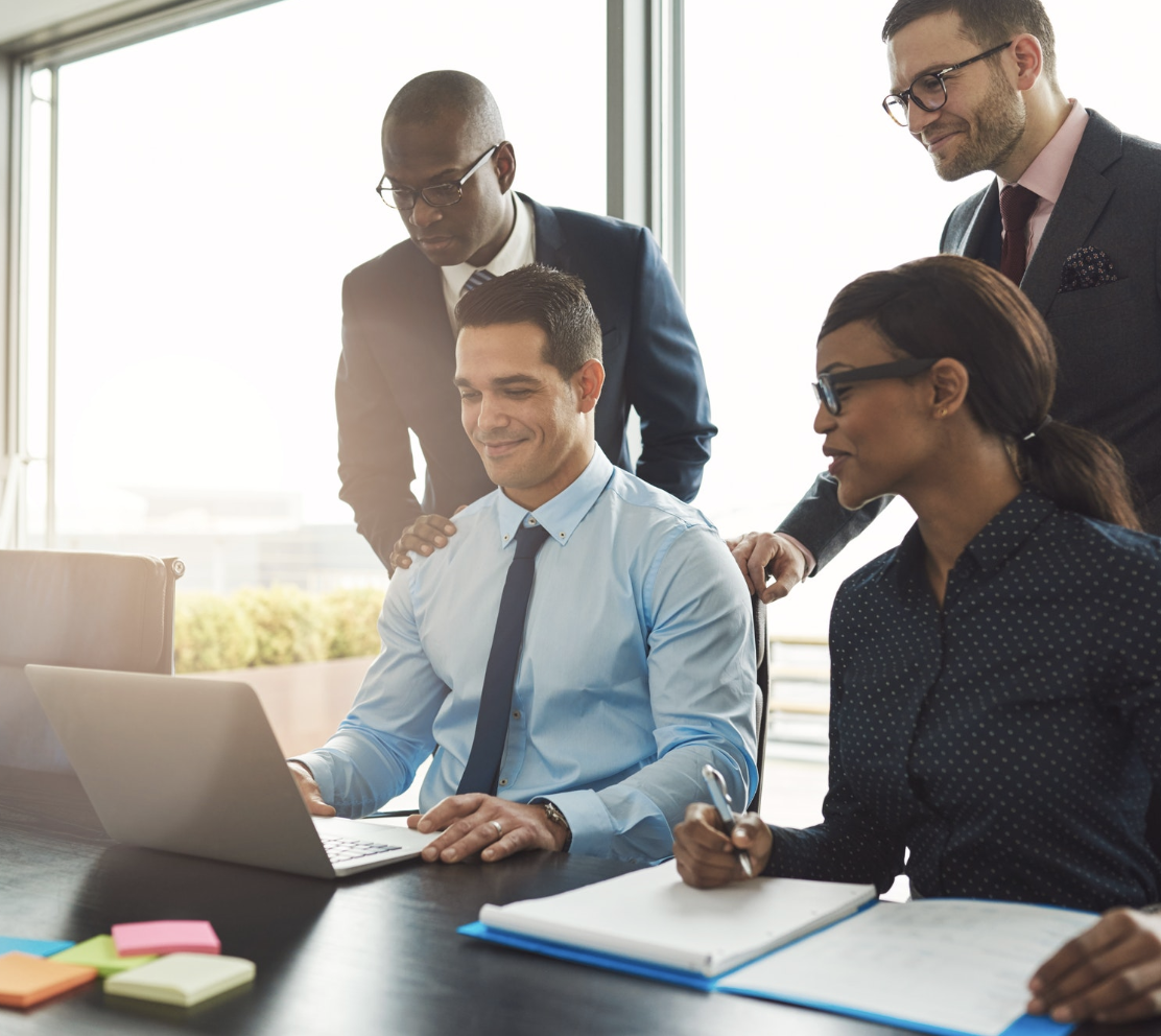 Diverse business team of four professionals gathered around laptop in modern office with windows